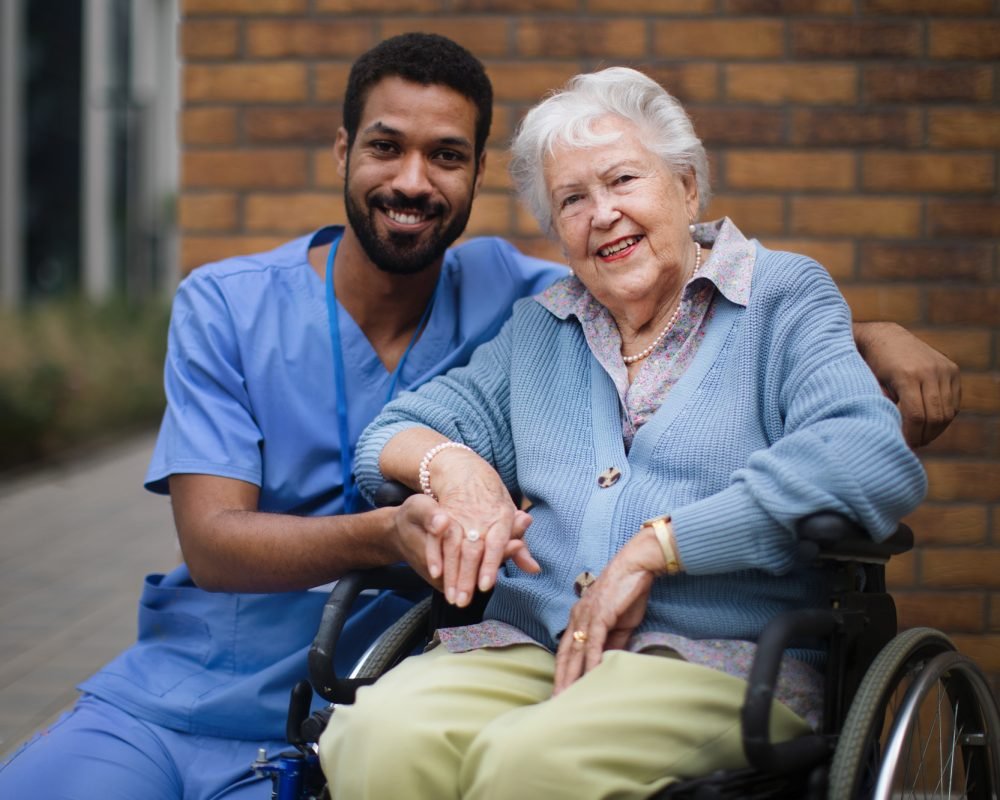 Happy senior woman at a wheelchair spending time outside with her assistant.